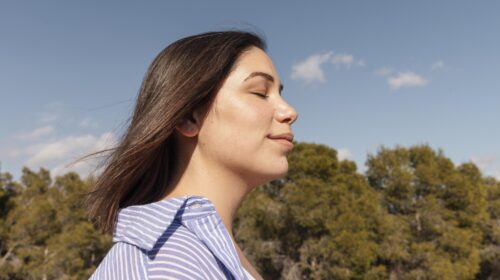 moça com os olhos fechados respirando em meio a natureza.