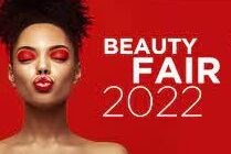 Imagem Beauty Fair 2022. Na direita temos uma mulher, negra com cabelos crespos preso e com maquiagem vermelha. Ao lado direito está escrito Beauty Fair 2022