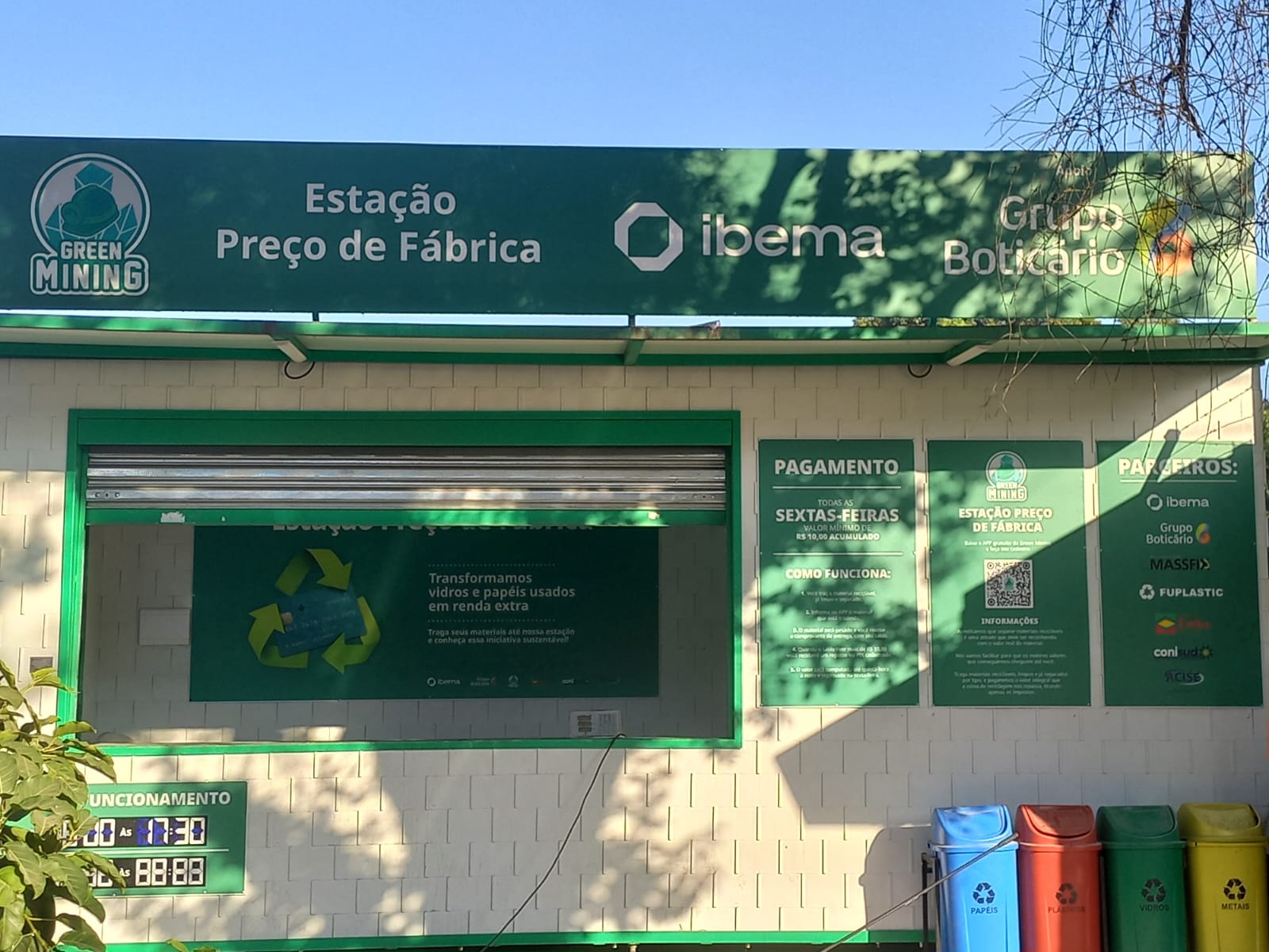 Estação de coleta de vidro e papel "Preço de Fábrica", imagem tirada da frente da estação de coleta à luz do dia