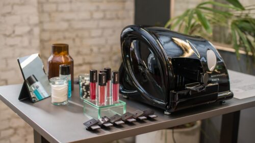 A display of multiple lipsticks arranged on a table alongside a stylish handbag and various bottles, showcasing products from Grupo Boticário.