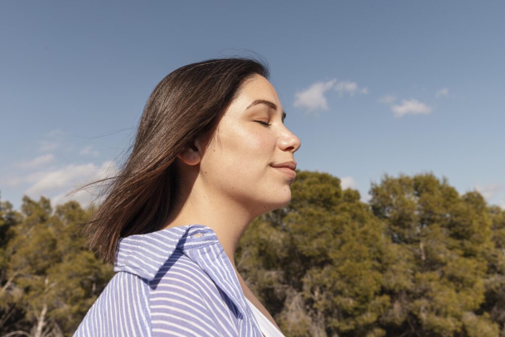 moça com os olhos fechados respirando em meio a natureza.